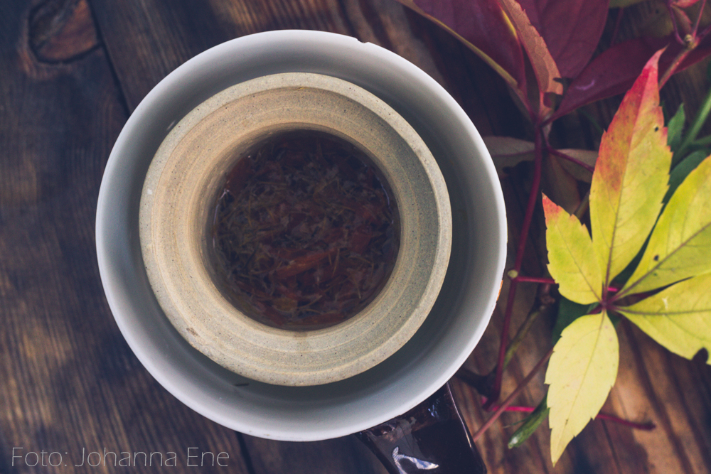 Tekopp och te-sil med te från trädgården.