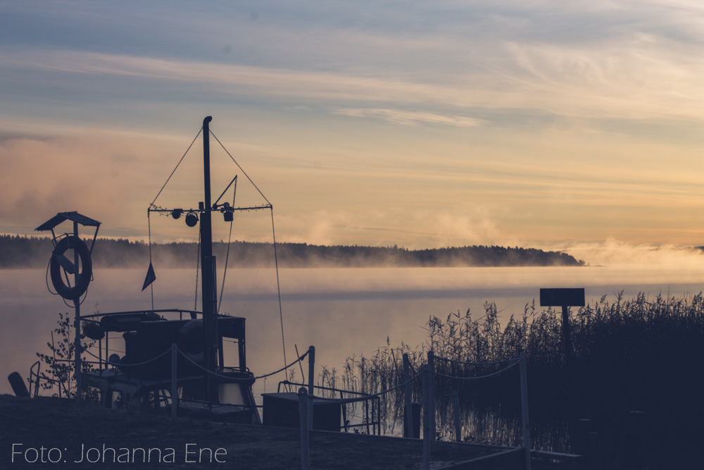 Båt vid brygga en tidig morgon med dimma över sjö.