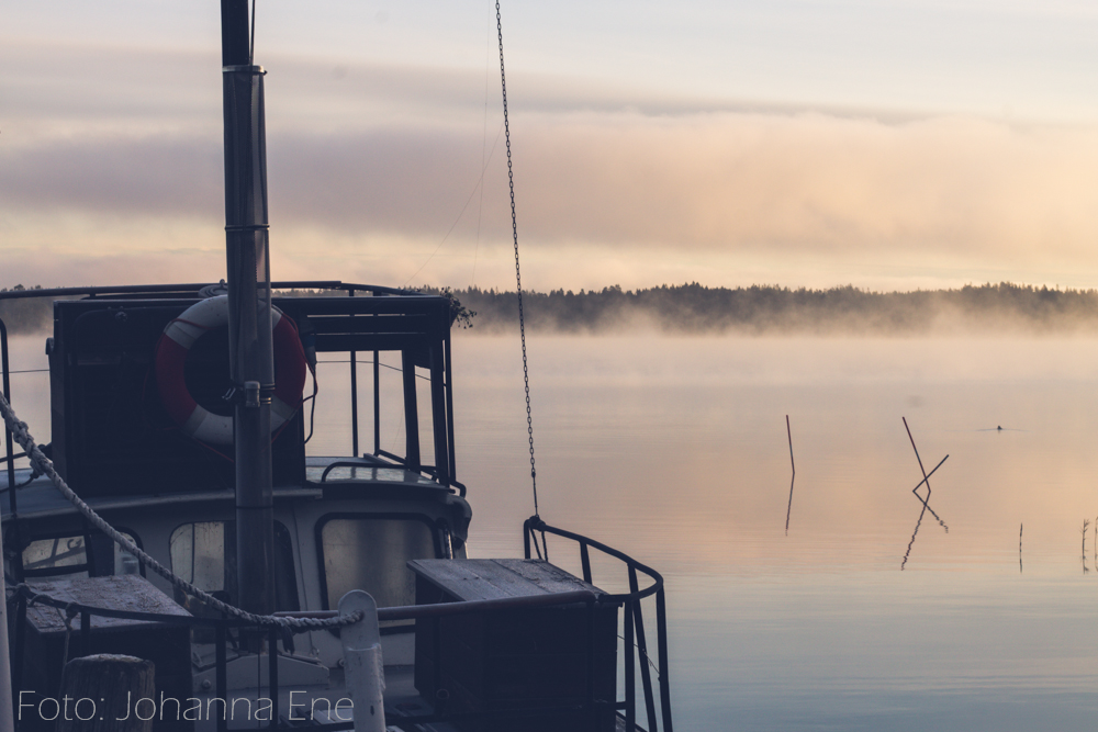 Båt vid brygga en tidig morgon med dimma över sjö.