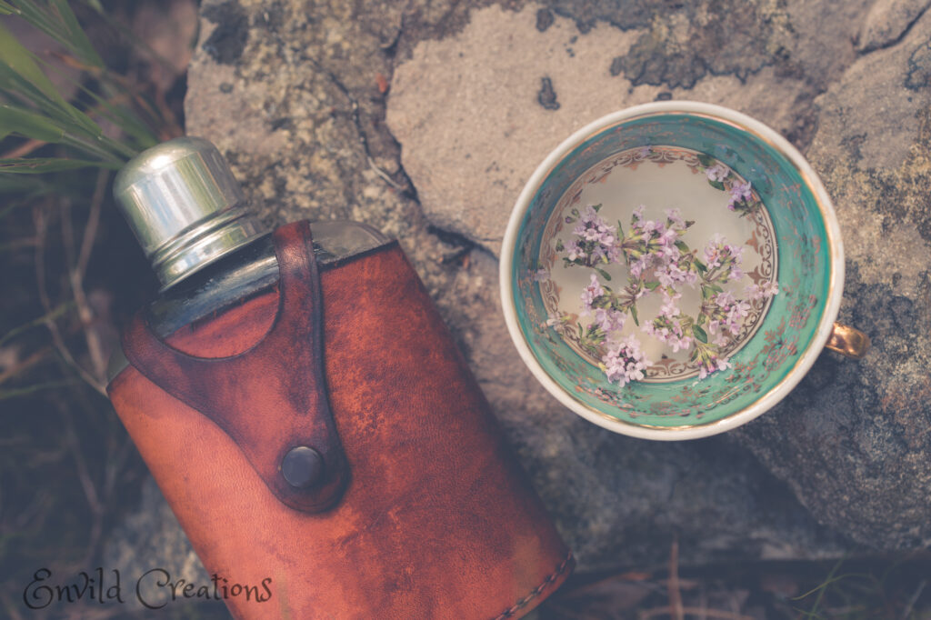 Plunta med läderfodral och gammal kaffekopp med blommor på bergshäll.